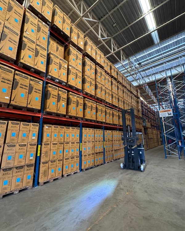 Porta-paletes do CD Maracanaú carregados até o teto, com empilhadeira ao fundo